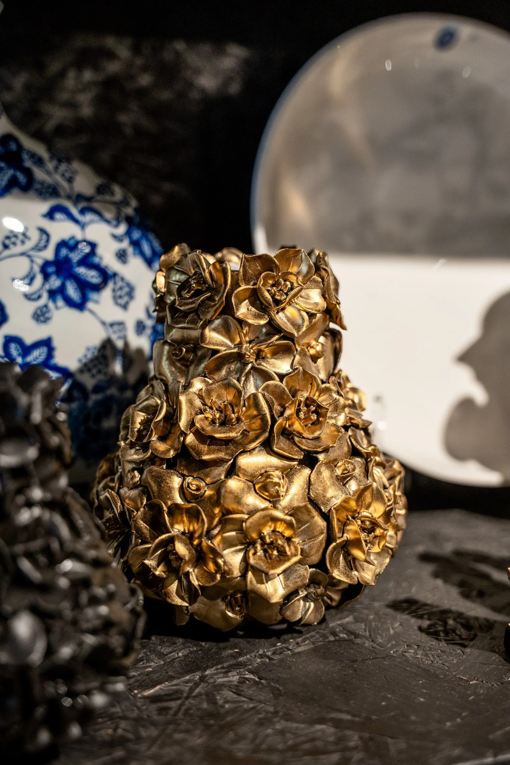 Een gouden vaas van keramieken rozen, tussen een zwarte en een blauw-witte vaas