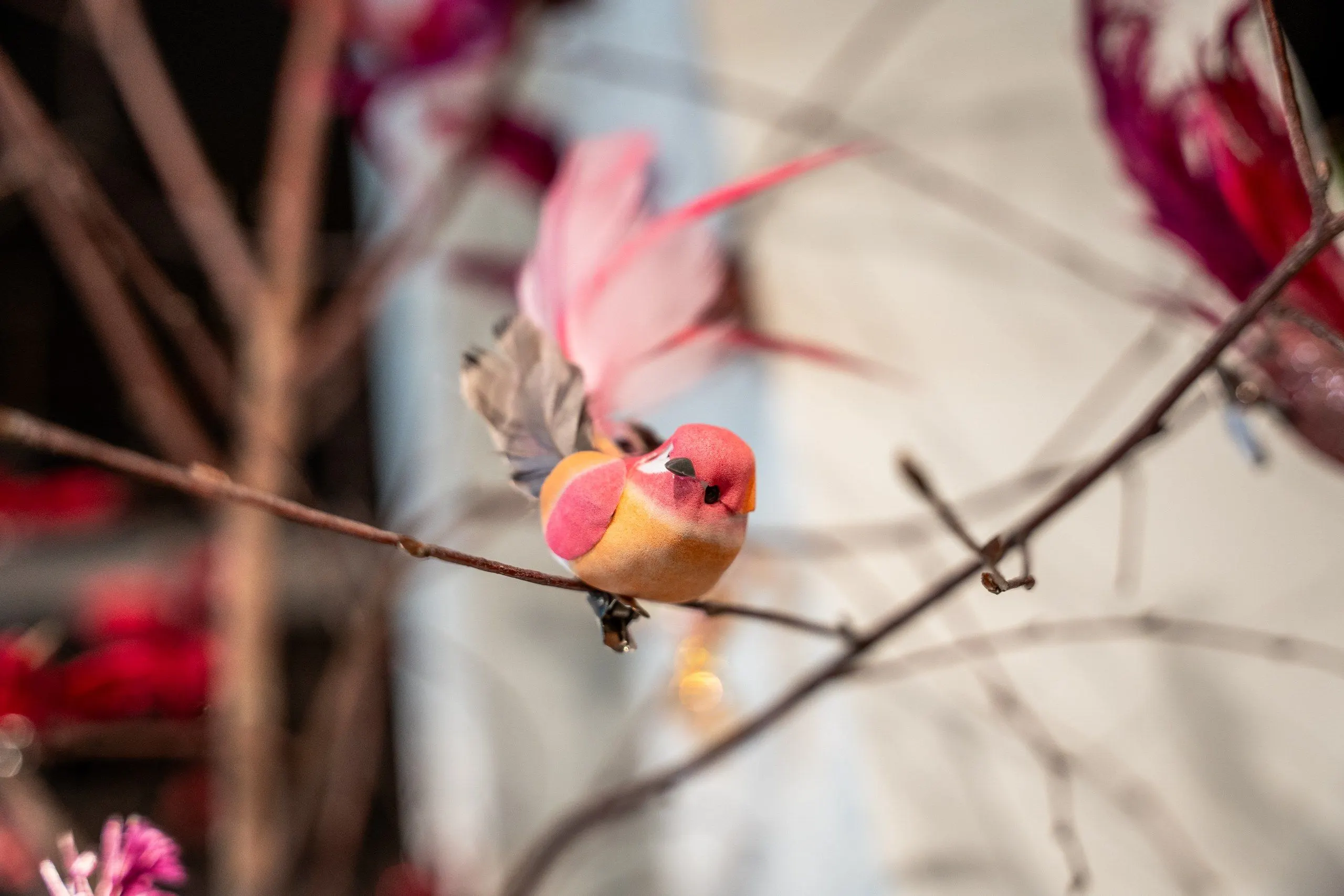 Een roze vogeltje op een kale tak, met zachte roze bloemen op de achtergrond