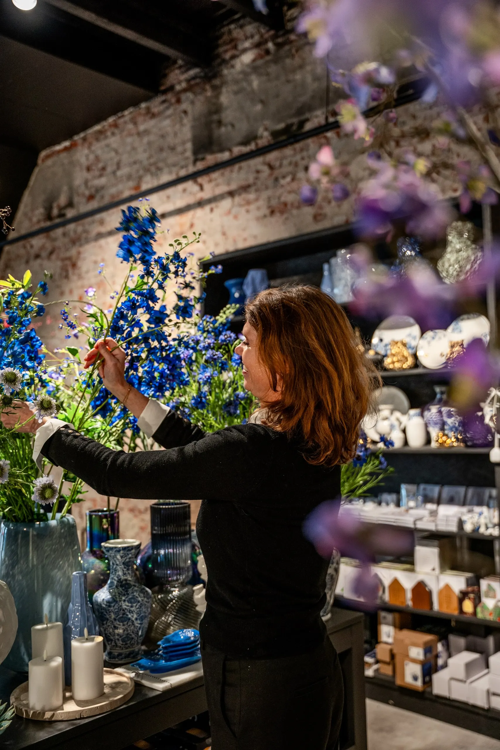 De eigenaresse schikt blauwe ridderspoor in een vaas, voor schappen met servies en vazen