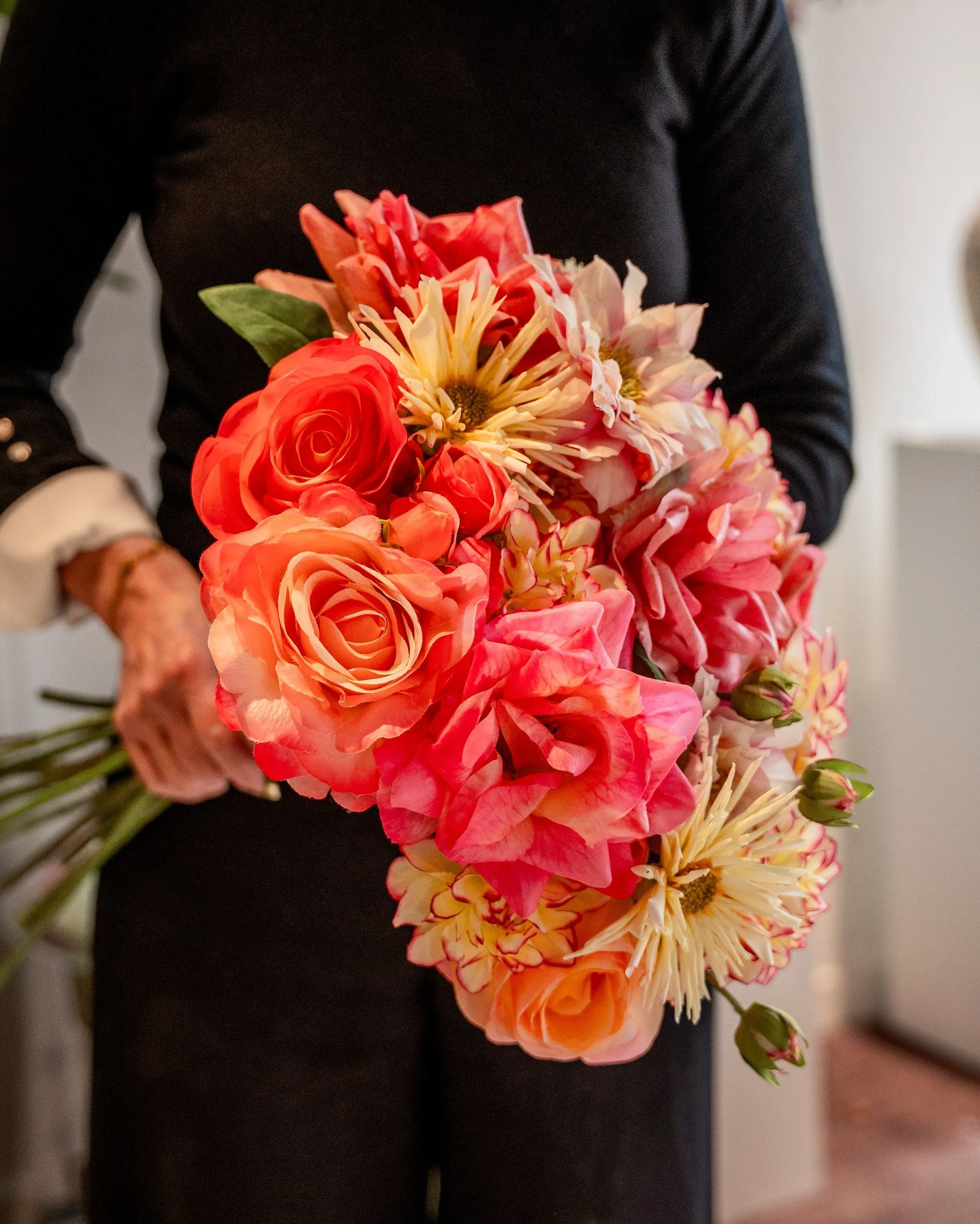 Boeket van koraalroze rozen en dahlia's met crèmekleurige cactusdahlia's, vastgehouden tegen een zwarte trui