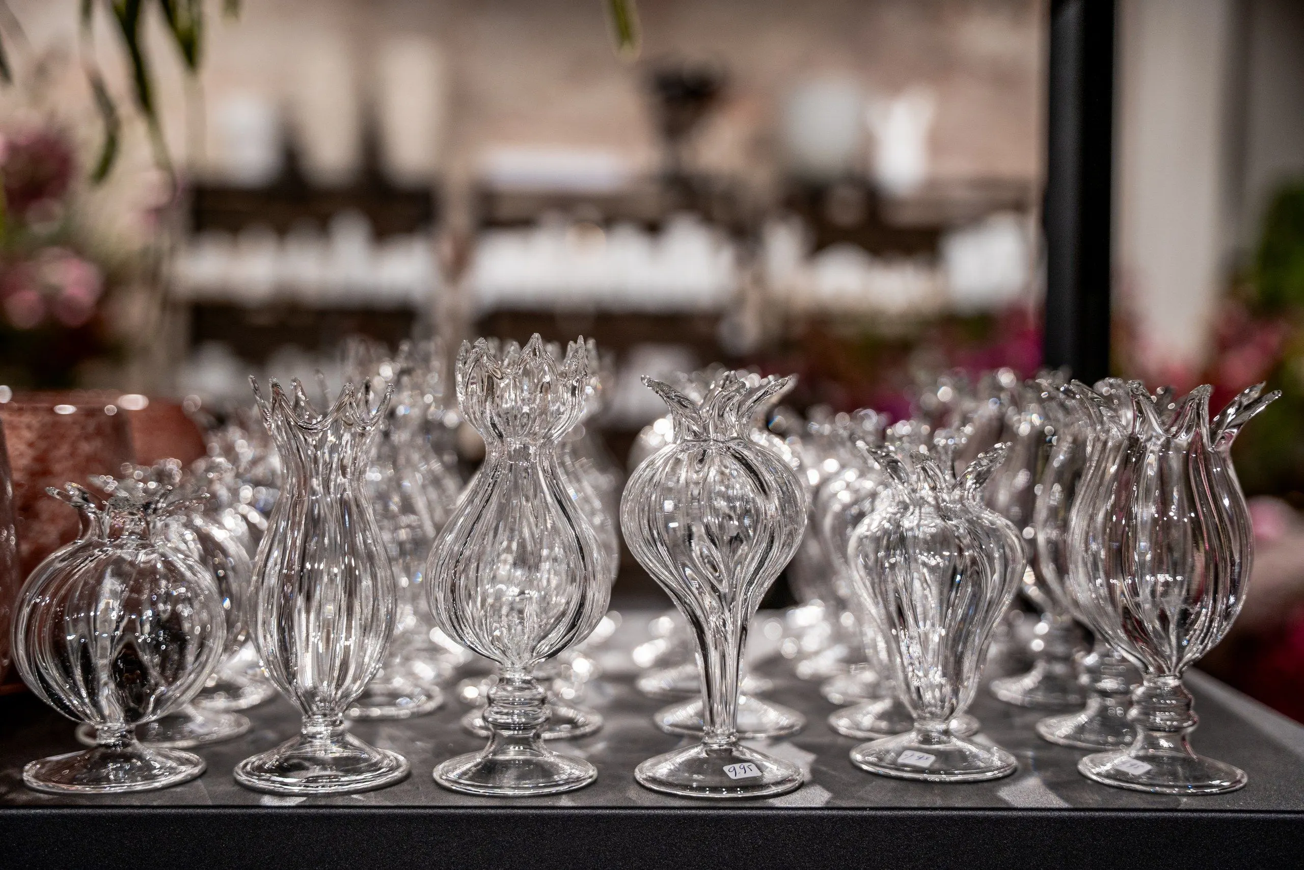 Rijen geribbelde glazen vaasjes met gekartelde randen, als bloemknoppen, op een donkere plank in de winkel